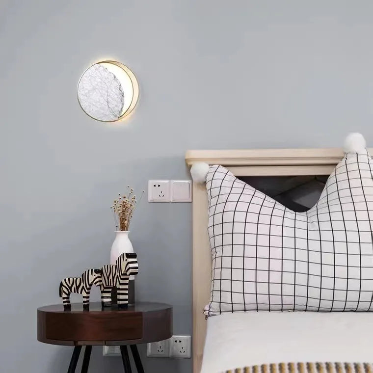 Bedroom interior with a zebra statue on a small table, round wall light, and bed with checkered pillow.