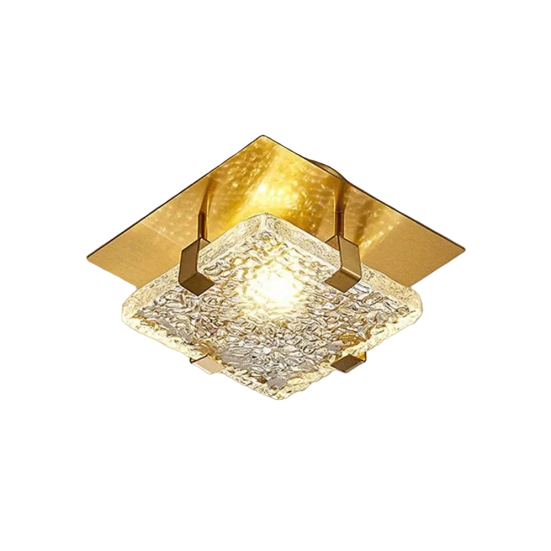 A modern square ceiling light fixture with a textured clear glass shade and a brushed gold metal frame, shown illuminated against a neutral background.
