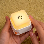 A person's hands holding a small square light-up switch device over a brown textured fabric background, with promotional text describing its light and click sound features.