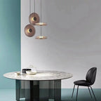 Modern dining table with marble top and black chair, featuring three hanging pendant lights.