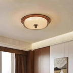 A round flush-mount ceiling light fixture with a warm wood frame and a ribbed glass shade, illuminated in a modern room setting.