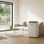 A white portable air conditioner or heater placed beside a sofa in a bright, modern living room with light wood floors, a large window, and a potted plant.