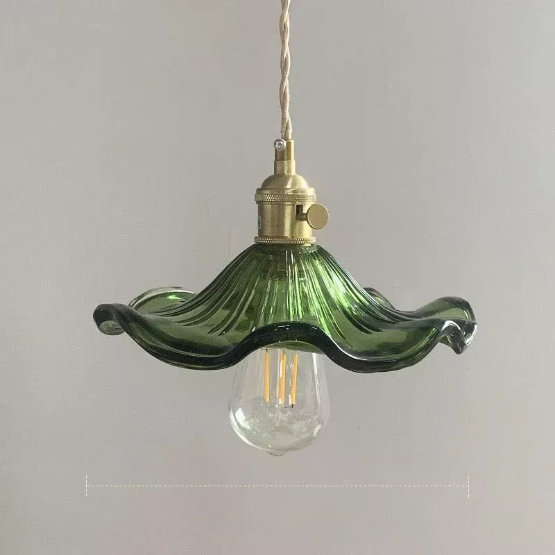 Green glass pendant light with brass fixture on a plain background